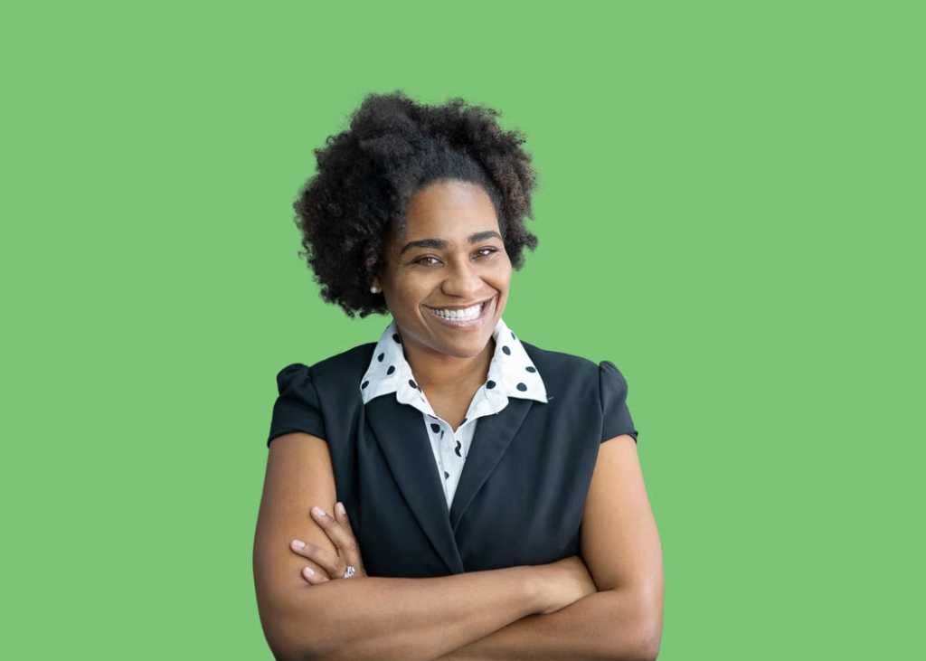 Portrait of a confident black woman with afro hair, posing against a green background in a studio.