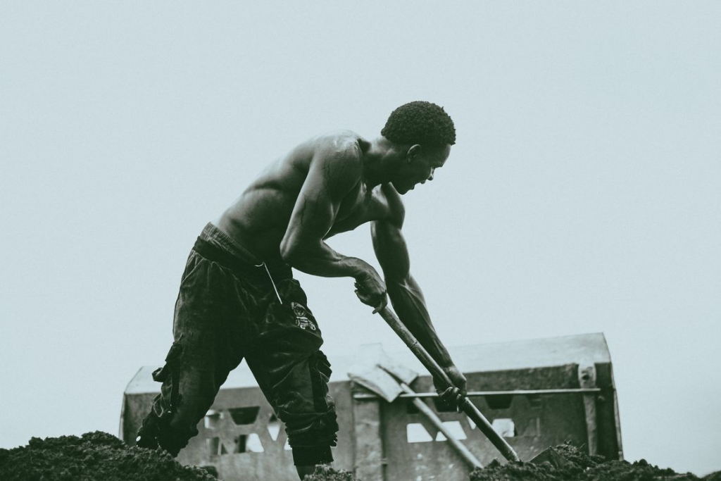 A strong shirtless man engaged in intense manual labor outdoors.